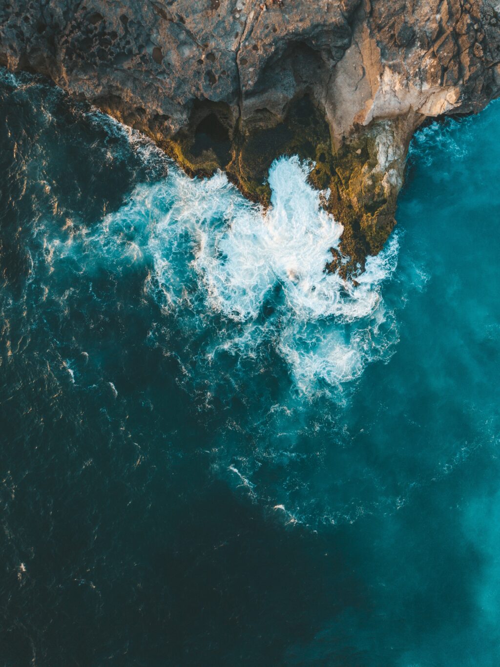 A vertical aerial shot of sea waves hitting the cliff